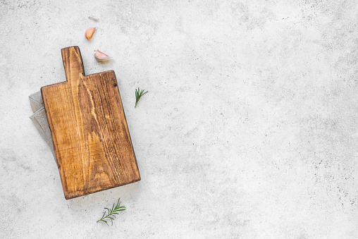 Empty wooden cutting board with napkin on white stone kitchen table, top view, flat lay. Wooden platter, copy space.
