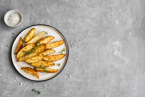 Roasted potato wedges with herbs and sea salt on plate, top view, copy space. Homemade oven baked potato snacks and sour cream sauce.