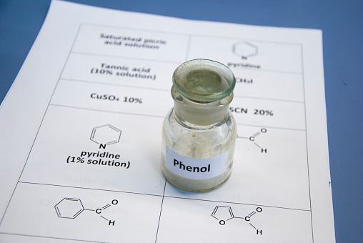 Phenol in old glass bottle on a sheet of paper with chemical formulae (selective focus)