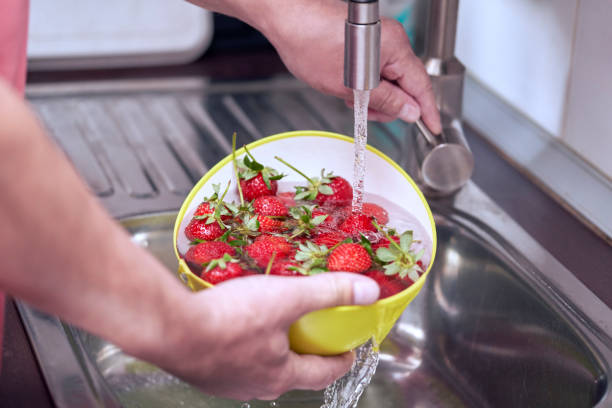 menschliche weiße hände halten eine schüssel erdbeeren über einer küchenspüle - washing fruit preparing food strawberry stock-fotos und bilder