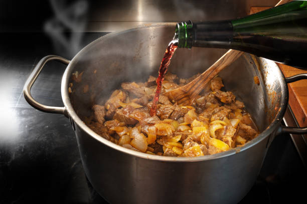 el vino tinto se vierte de una botella en una olla con goulash asado para desglase, cocinando en el concepto casero, enfoque seleccionado - fried onion roasted chopped fotografías e imágenes de stock