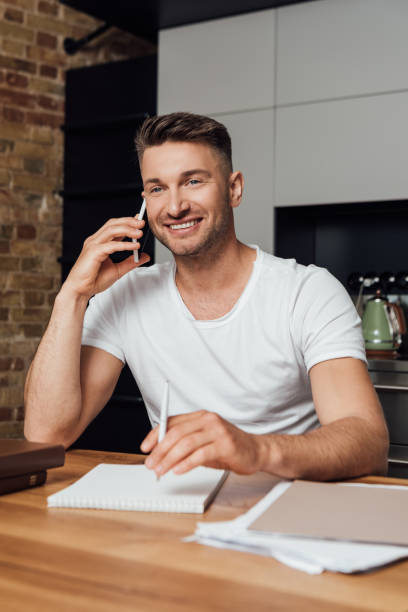 istock Selective focus of smiling man talking on smartphone near notebook and paperwork on table at home 1250959456