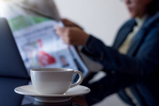 Happy young woman drinking coffee and reading newspaper at cafe