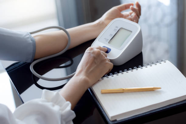 Measuring blood pressure Woman measuring blood pressure by using digital sphygmomanometer with empty white notebook or diary on the desk at home. Medical and healthcare concept. monitoring equipment photos stock pictures, royalty-free photos & images