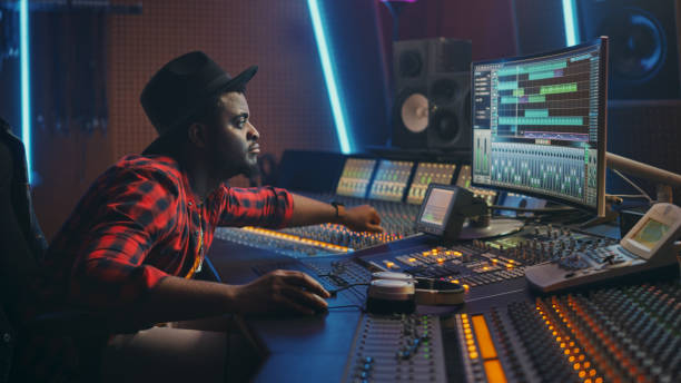 istock Stylish Audio Engineer Working in Music Recording Studio, Uses Mixing Board and Software to Create Modern Hit Song. Creative Black Artist Musician Working on Desk Control Surface to Produce New Song 1250963230