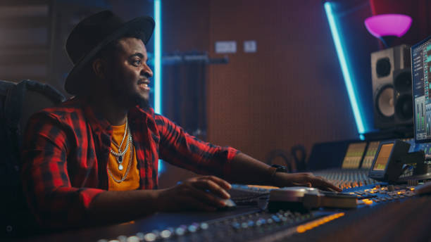 istock Stylish Audio Engineer / Producer Working in Music Recording Studio, Uses Mixing Board and Software to Create Modern Hit Song. Black Artist Musician Using Control Desk to Produce New Song. 1250963231