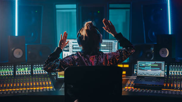 Artist, Musician, Audio Engineer, Producer in Music Record Studio, Uses Control Desk with Computer Screen showing Software UI with Song Playing. Celebrates Success with Raised Hands, Dances. Back View