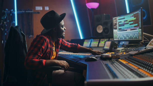 istock Portrait of Audio Engineer Working in Music Recording Studio, Uses Mixing Board Create Modern Sound. Successful Black Artist Musician Working at Control Desk. Having Fun, Smiling. 1250963258