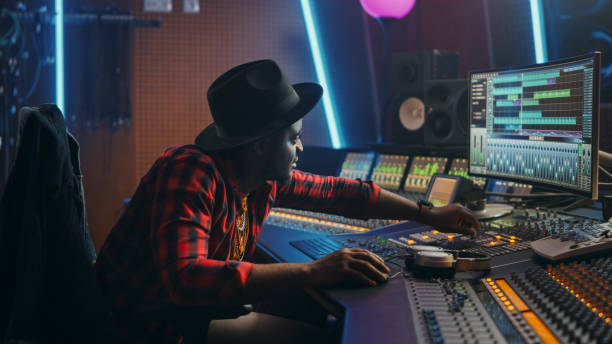 istock Portrait of Audio Engineer Working in Music Recording Studio, Uses Mixing Board Create Modern Sound. Successful Black Artist Musician Working at Control Desk. Having Fun, Smiling. 1250963262
