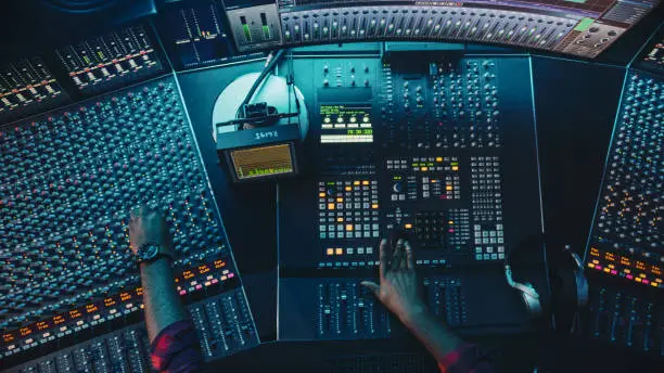 Photo of Audio Engineer, Musician, Artist Works in the Music Record Studio, Control Desk Mixer with Equalizer. Hand Moving Fader, Buttons to Broadcast, Record, Play Song. Neon Colors. Top Down View