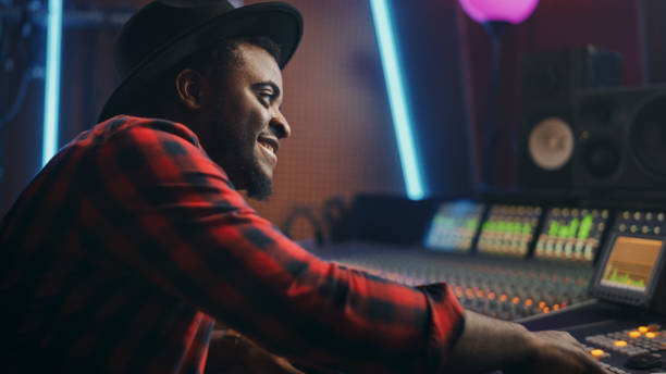 istock Portrait of Audio Engineer Working in Music Recording Studio, Uses Mixing Board Create Modern Sound. Successful Black Artist Musician Working at Control Desk. Having Fun, Smiling. 1250963292