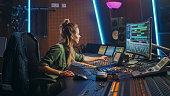Beautiful Female Audio Engineer Working in Music Recording Studio, Uses Mixing Board and Software to Create Modern Sound. Creative Girl Artist Musician Working on Control Desk to Produce New Song