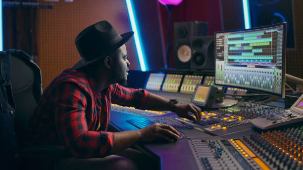 istock Stylish Male Audio Engineer Working in Music Recording Studio, Uses Mixing Board, Software to Create Modern Hit Song. Creative Artist Musician Working on Workdesk Control Surface to Produce New Song 1250963328
