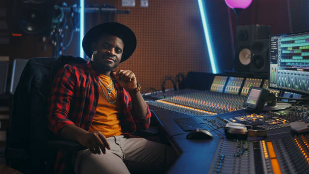 istock Stylish Audio Engineer Working in Music Recording Studio, Uses Mixing Board and Software to Create Modern Hit Song. Looking at Camera Portrait of Black Artist Musician Working at Control Desk 1250963332