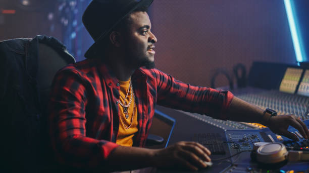 Stylish Audio Engineer / Producer Working in Music Recording Studio, Uses Mixing Board and Software to Create Hit Song. Creative Black Artist Musician Using Control Desk to Produce New Track. elegante ingeniero de audio / productor que trabaja en el estudio de grabación de música, utiliza la mesa de mezcla y el software para crear la canción de éxito. artista negro creativo músico usando control desk para producir nueva pista.