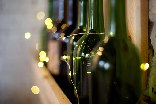 Yellow Christmas garland and green wine bottles on a wooden shelf, horizontally