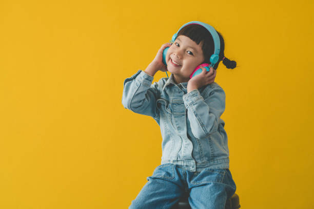 Cute Asian little girl enjoy and listening music in headphones on the yellow wall background Cute Asian little girl enjoy and listening music in headphones on the yellow wall background double denim stock pictures, royalty-free photos & images