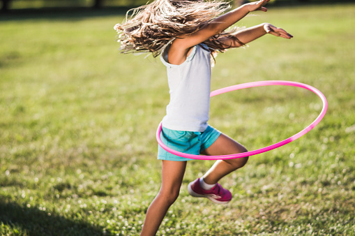 Beautiful girl is playing with hula hoop in the public park.