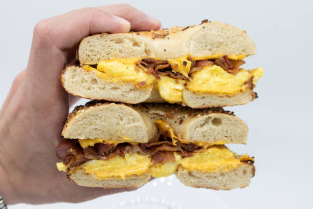 istock Hand Held Everything Bagel Cut in Half with Bacon Eggs and Cheese with a White Background 1250970280