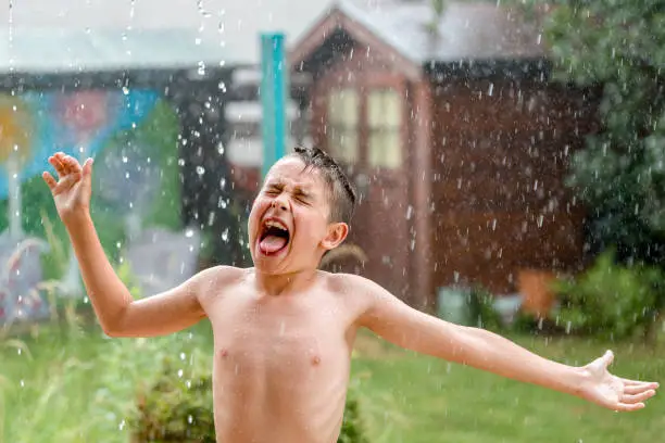 boy in the garden with a colorful background
playing in the rain, child getting wet from the raindrops, happy kid dancing, rain drops