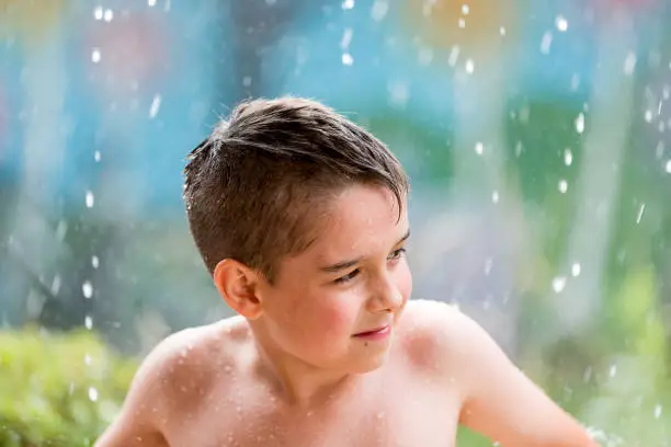 boy in the garden with a colorful background
playing in the rain, child getting wet from the raindrops, happy kid dancing, rain drops