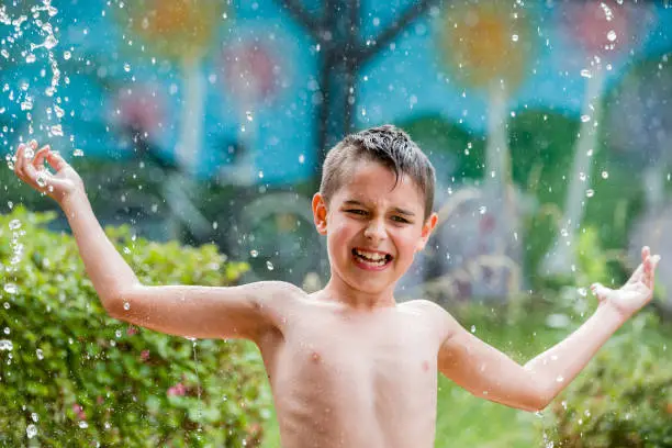 boy in the garden with a colorful background
playing in the rain, child getting wet from the raindrops, happy kid dancing, rain drops