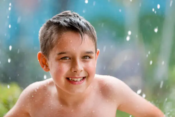 boy in the garden with a colorful background
playing in the rain, child getting wet from the raindrops, happy kid dancing, rain drops