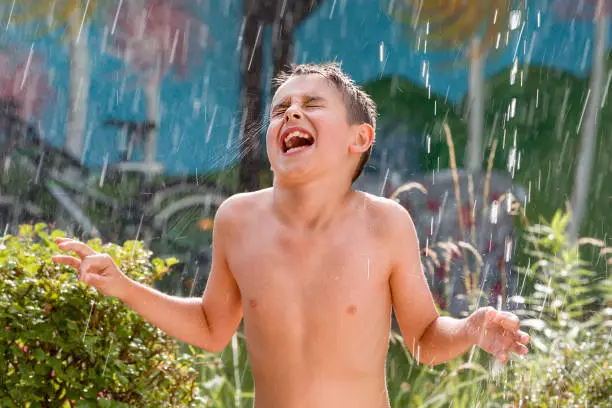 boy in the garden with a colorful background
playing in the rain, child getting wet from the raindrops, happy kid dancing, rain drops