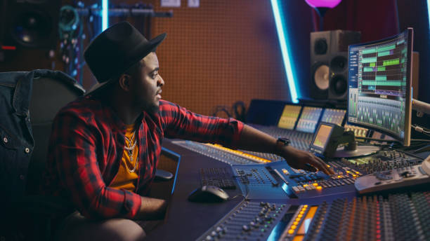 istock Stylish Audio Engineer Working in Music Recording Studio, Uses Mixing Board and Software to Create Modern Hit Song. Creative Black Artist Musician Working on Desk Control Surface to Produce New Song 1250975204