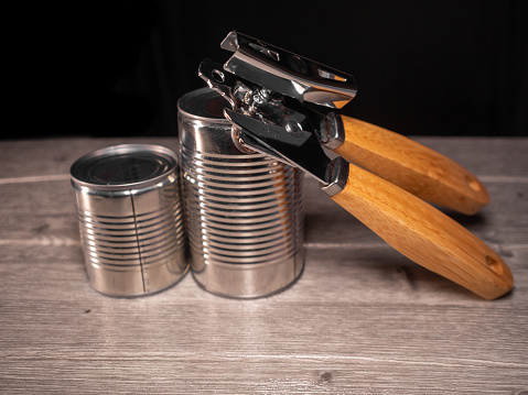 two canned aluminum products with a stainless steel and wooden can opener a wooden board and a black background