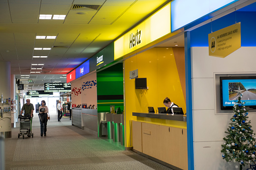 Christchurch, New Zealand - December 30, 2018. Travelers walking in the terminal of Christchurch Airport with a lady standing behind Hertz car rental counter, Christchurch, New Zealand.