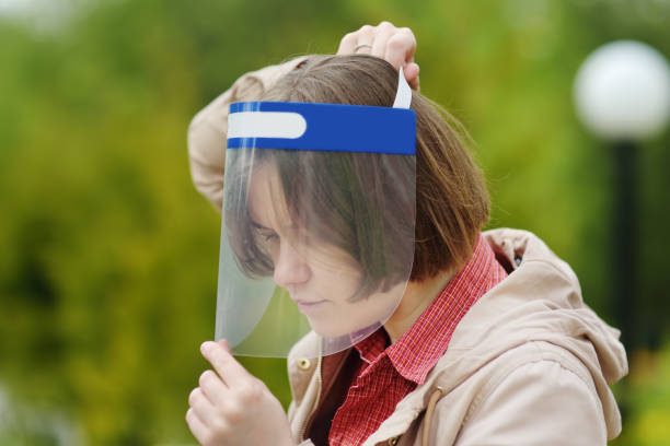 Young woman putting on face shield on street of city or public park. Safety during COVID-19 outbreak.Lifting virus lockdown. Social distancing and face mask - security measures when exiting quarantine mujer joven poniéndose protector facial en la calle de la ciudad o el parque. seguridad durante el brote de covid-19. levantar el bloqueo del virus. distanciamiento social y máscara facial - medidas de seguridad al salir de la cuarentena