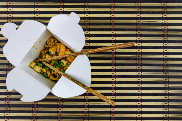 Paper box with pad thai and chopsticks on bamboo mat. Top view