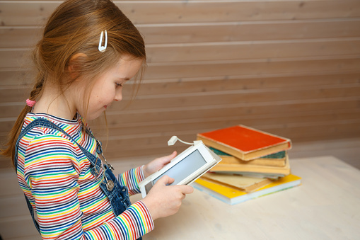 A little girl sits at a table and reads an e-book.