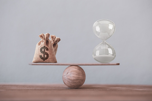 Write sand clock or hourglass symbol and dollar bagson a balance scale in equal position. Financial concept : Time value of money, asset growth over time, depicts investment in long-term equity for more money growth
