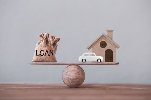Loan bags, wood home with car in a house on balance scale. Concept family financial management, mortgage and payday loan or cash advance.