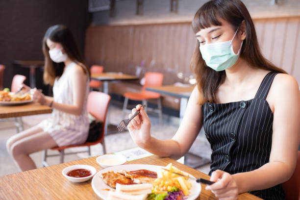 Asian woman sitting separated in restaurant eating food .keep social distance for protect infection from coronavirus covid-19, restaurant and social distancing concept. Asian woman sitting separated in restaurant eating food .keep social distance for protect infection from coronavirus covid-19, restaurant and social distancing concept. food court photos stock pictures, royalty-free photos & images