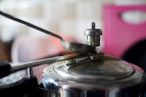 Pressure cooker in an indian kitchen with the whistle pressure release valve held open with a spoon stock photo