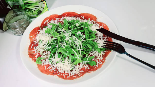 istock Beef carpaccio with greens and parmesan on white plate with knife and fork 1250989996