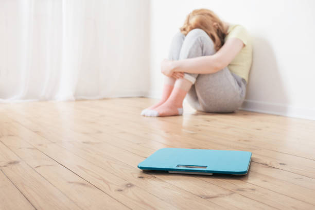 sad teenager girl with scale on wooden floor sad teenager girl with scale on wooden floor bulimia stock pictures, royalty-free photos & images