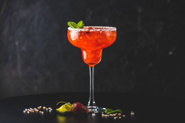 Frozen strawberry lime mint margarita in tall footed glass on the dark background. Luxury alcohol fresh drink stock photo