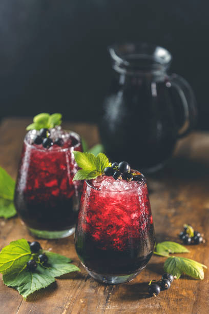 two glass of cold ice black currant juice or cocktail with ripe berries and green leaves on dark wooden table. alcohol or non alcohol summer fresh drink - vitality food food and drink berry fruit imagens e fotografias de stock