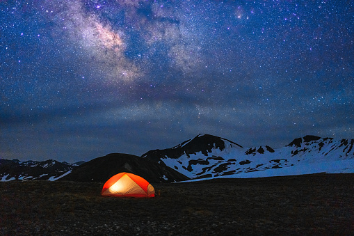 Backpacking Tent Glowing Under Night Sky and Milky Way - Outdoors adventure with glowing orange tent with sky full of stars and crisp Milky Way Galaxy. Colorado Rocky Mountains, Aspen, Colorado USA.