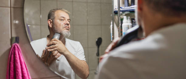 istock Man looking at mirror and shaving beard with trimmer 1250999104