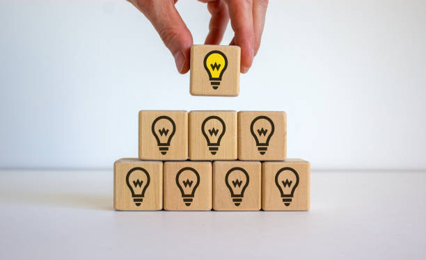 istock Male hand placing a cube with light bulb sign on top of a pyramid. White table. Beautiful white background, copy space. Business concept. 1251000115