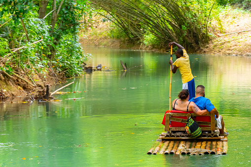 Falmouth, Jamaica - July 07 2019: Tourists on bamboo raft ride on Martha Brae River. Relaxing scenic tour through countryside landscape under canopy of trees. People enjoy summer vacation activity.