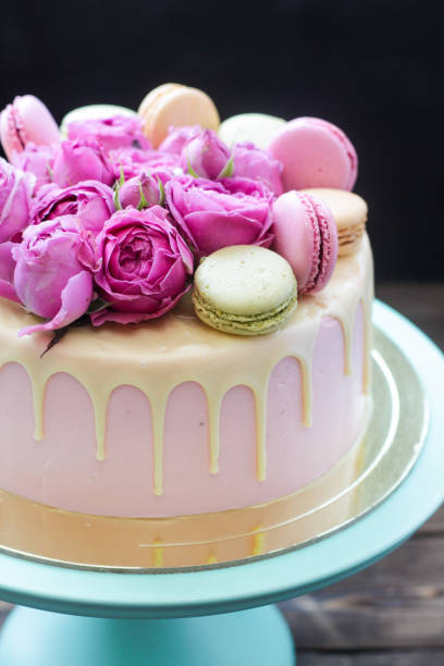 istock Elegant pink wedding cake decorated with melted white chocolate, beautiful fresh roses and macaroons. Black background. 1251002986