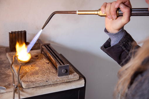 A Jewelry designer using a blowtorch to melting down silver pellets to shape into a ring.