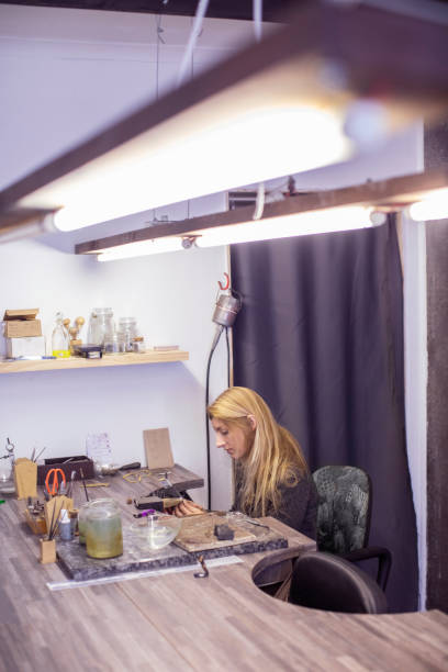 a jewelry designer working on a piece of jewelry at her workbench. - thirty pieces of silver imagens e fotografias de stock