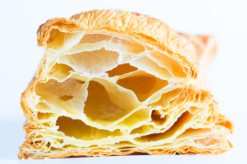 A closeup image  of puff pastry in the incision with blown large crunchy layers of golden brown crust on top visible. Located on the center side on white background